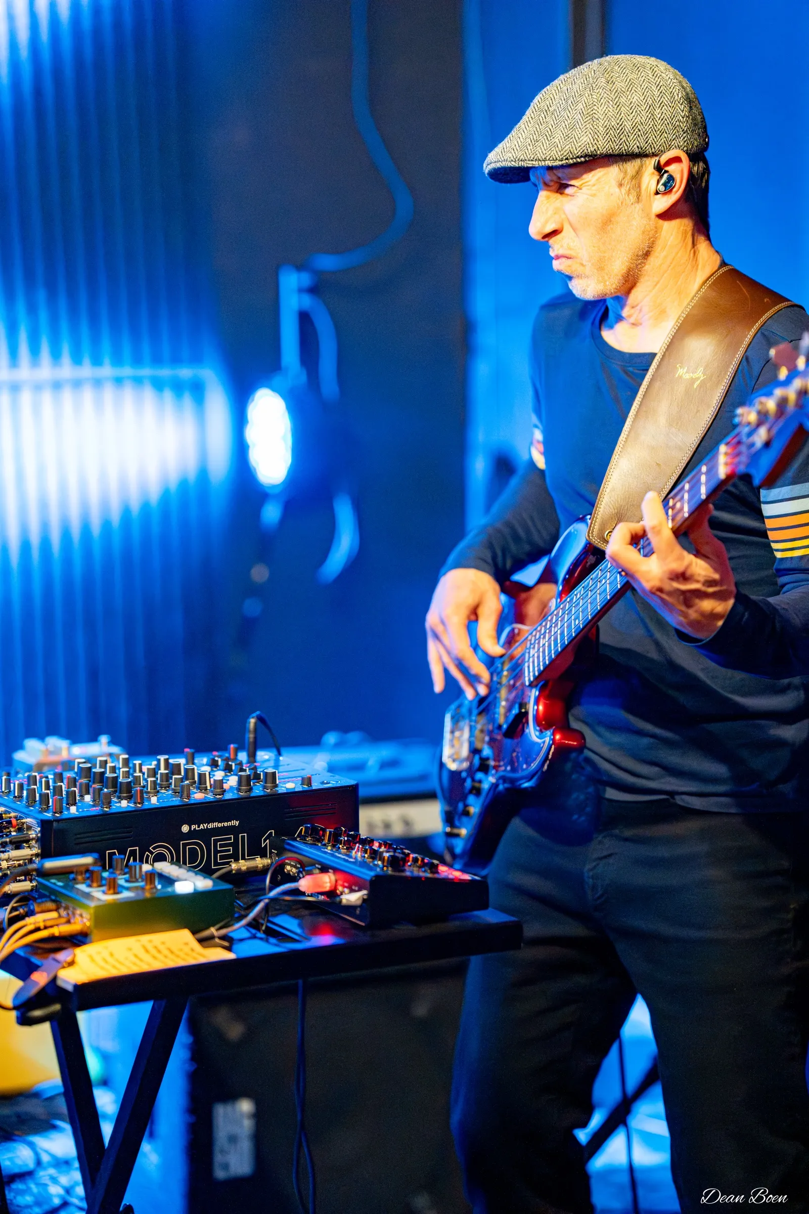 Bassist playing beside a table of synths under blue stage light