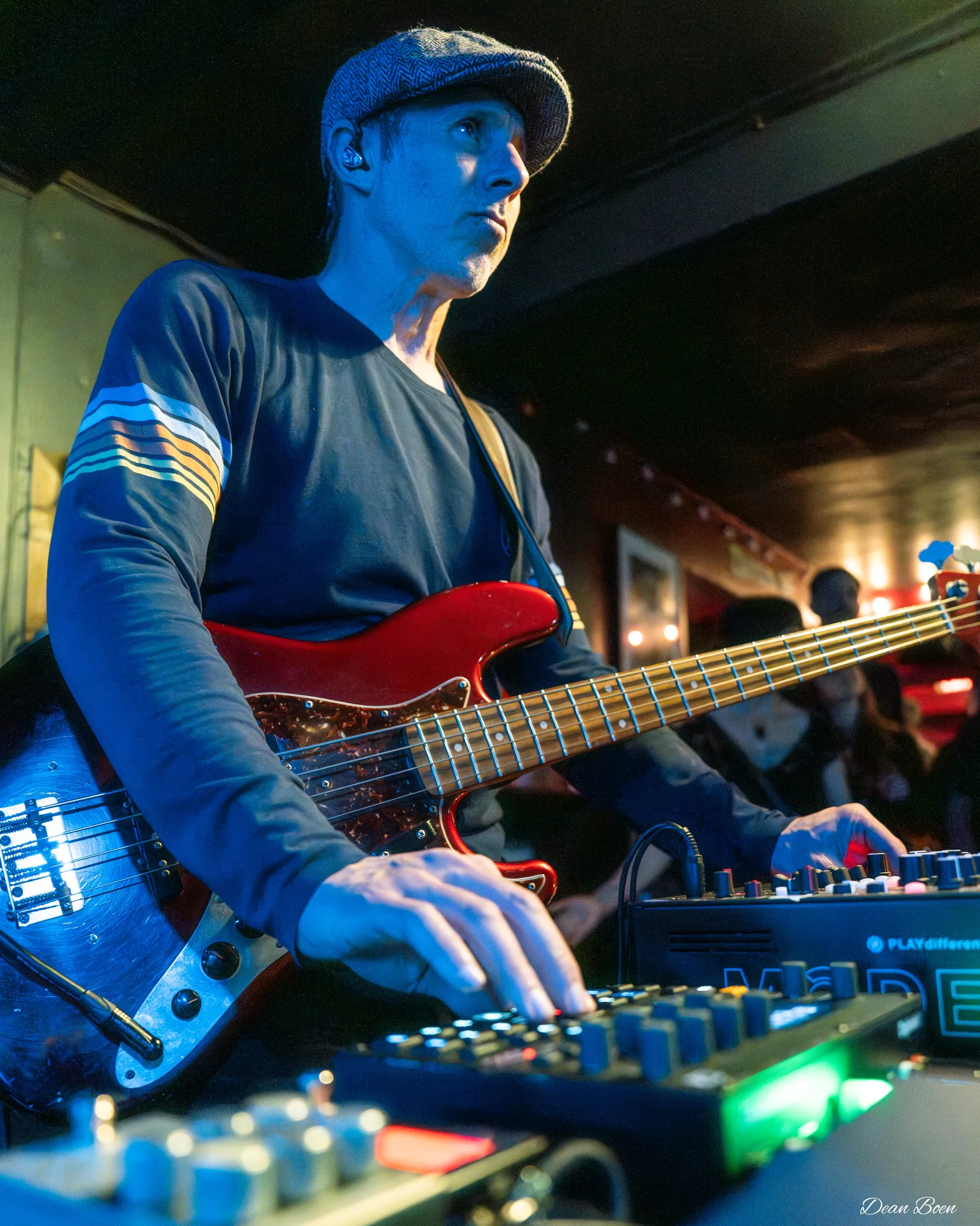 Bassist with a red bass playing a synth with one hand
